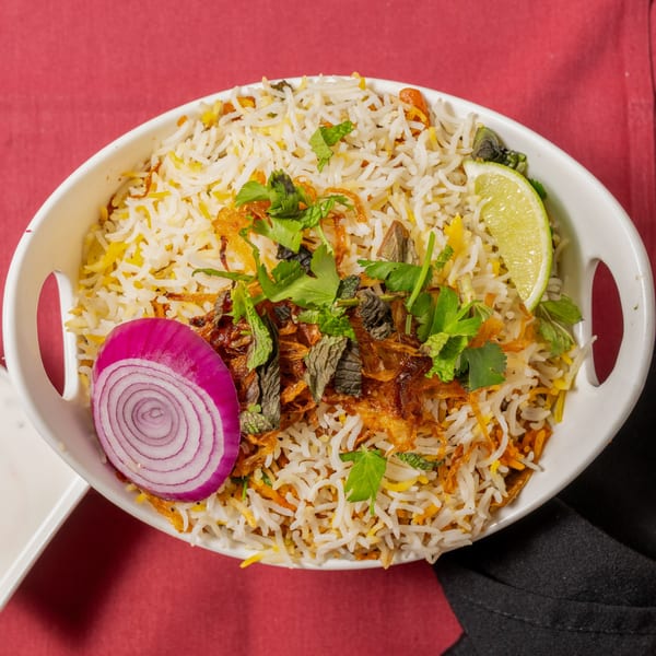 A white bowl of biryani rice with fried onions, herbs, a red onion slice, and lime.