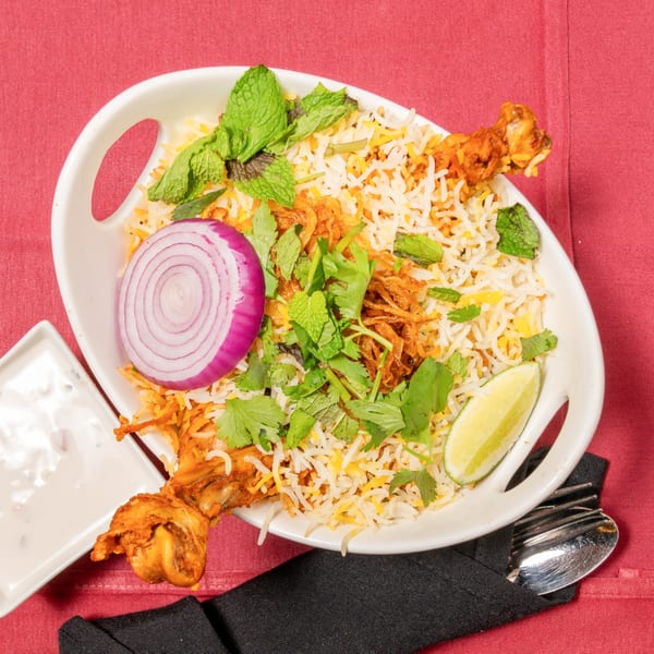 Chicken biryani with rice, mint, cilantro, red onion, and lime, served with raita.