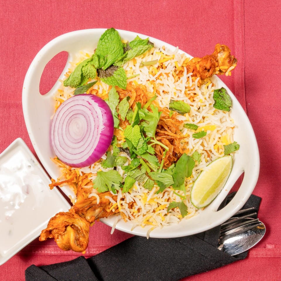 Chicken biryani with rice, mint, cilantro, red onion, and lime, served with raita.