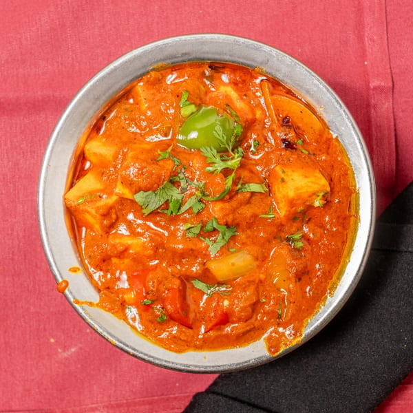 A close-up, overhead view of a metal bowl filled with paneer butter masala, garnished with cilantro.