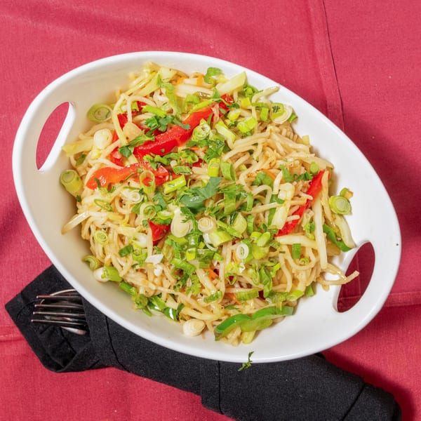 Noodle dish with red peppers, green onions, and cilantro in a white bowl on a red tablecloth.