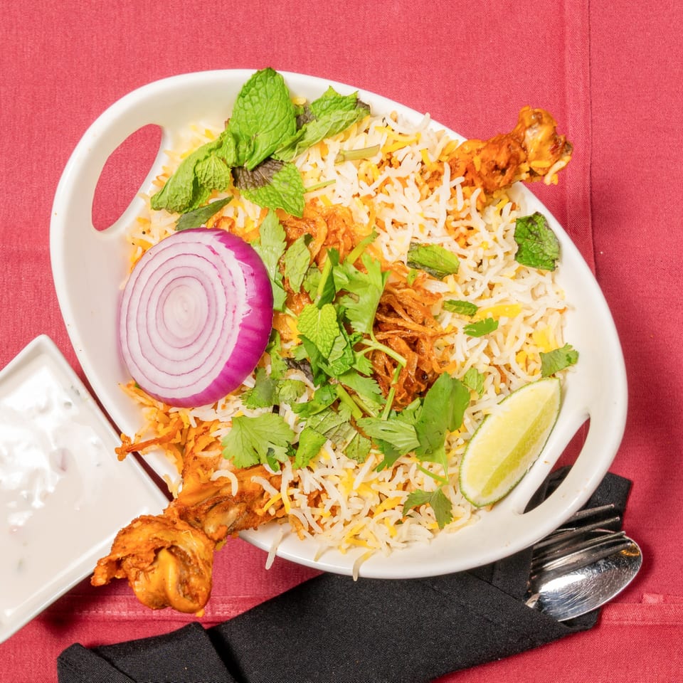 Chicken biryani with rice, red onion, mint, cilantro, and lime, served with raita.