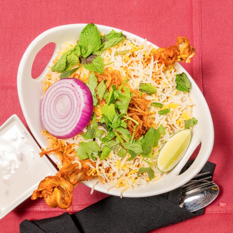 Chicken biryani with rice, red onion, mint, cilantro, and lime, served with raita.