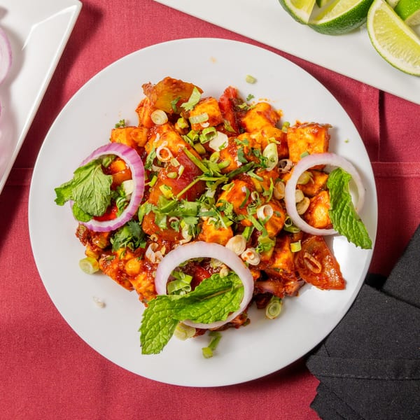 Spicy paneer dish garnished with red onion rings, mint leaves, and chopped green onions.