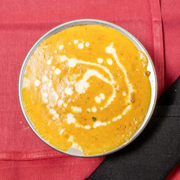 Overhead view of a metal bowl filled with creamy orange curry, drizzled with white cream swirls.