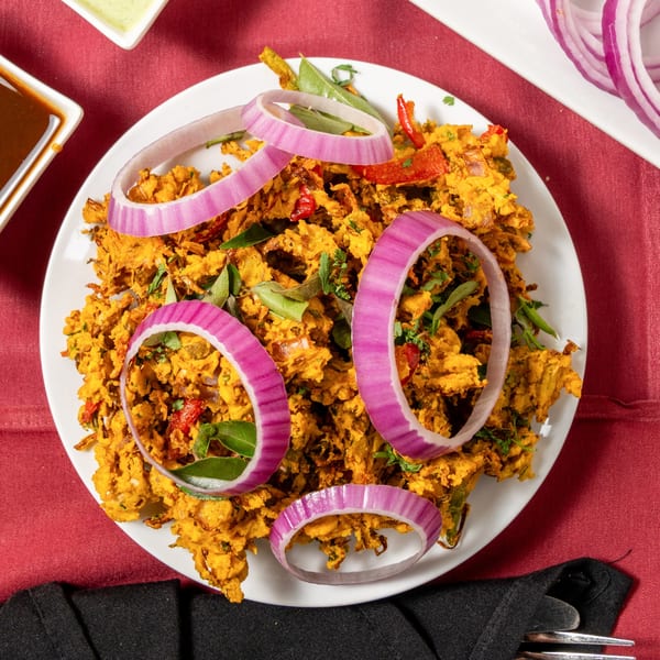 Crispy golden pakora, garnished with fresh curry leaves and vibrant red onion rings, on a white plate.