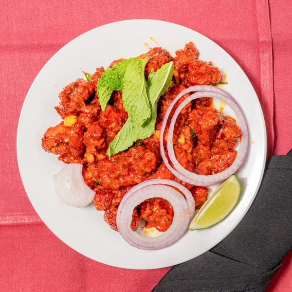 Spicy red chicken dish garnished with mint, red onion rings, and a lime wedge on a white plate.