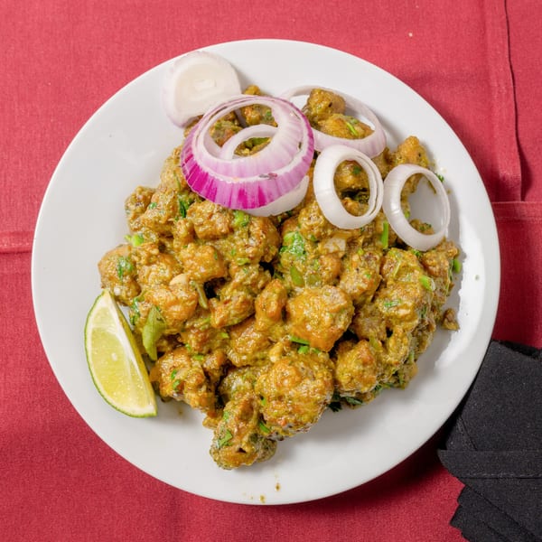 A plate of green chili chicken, garnished with red onion rings and a lime wedge, on a red tablecloth.